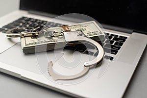 Cyber crime legal law police handcuffs on a hundred dollar bills with computer keyboard technology of criminal taking