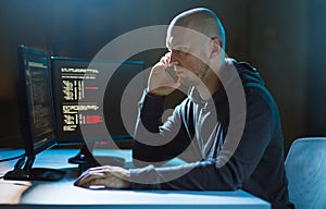 Hacker with program on computer calling on cell