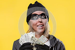 Cybercrime and money theft. A woman in a hat, gloves and mask holds a wad of money in her hands and looks up dreamily. Yellow