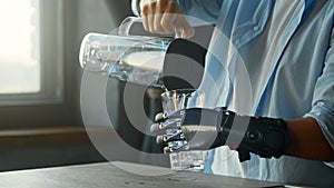 Cyborg guy with artificial limb pours water into glass from large bowl and drinks standing in kitchen