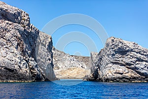 Cyclades Greece. Rock formation, cliff and cave, rippled Aegean Sea and blue sky, near Ios island