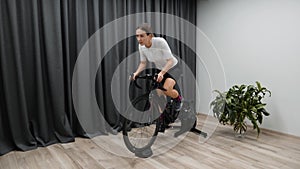 Cycle indoors at home on stationary bicycle trainer woman pedaling out of saddle as a part of race preparation. Pro cycling