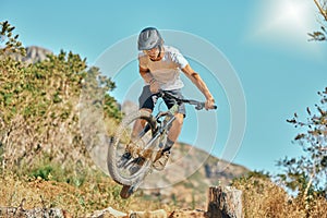 Cycling, jumping and man on bicycle in the countryside for fitness, stunt and freedom on blue sky background. Nature