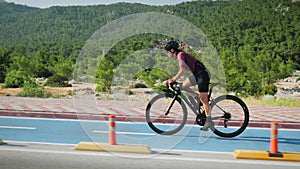 Cycling training. Young brunette female cyclist in black helmet and cycling apparel riding bicycle on bicycle lane in sunny mornin