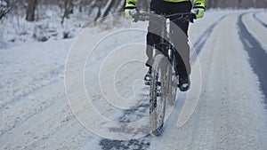 Cycling in the winter through a snowy forest. The cyclist rides on a slippery asphalt road. Male feet are pedaling. A