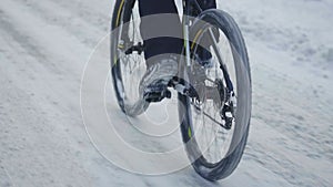 Cycling in the winter through a snowy forest. The cyclist rides on a slippery asphalt road. Male feet are pedaling. A