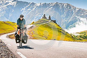 Cyclist back view on the road in scenic caucasus nature with Gergeti trinity monastery in the background. Traveller on bicycle.