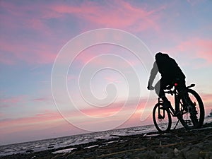 Cyclist on the background of a winter sunrise on the sea coast