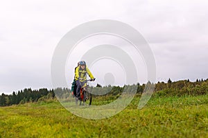 Cyclist backpacker rides on a dirt road through a field