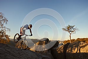 Cyclist balancing on front wheel on trial bicycle on boulder