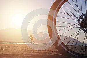 A cyclist behind a big bike wheel on the beach