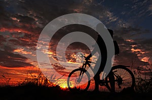 Cyclist with a bicycle, in the background fiery sunset