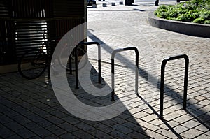 Five wheel stands of black metal bent tube in the shape of a rectangle in front of the retaining wall paving of granite cubes in