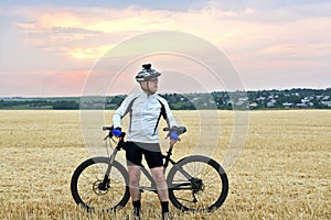 The a cyclist with the bike resting on straw harvested field