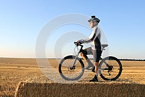 Cyclist with the bike resting on straw harvested field