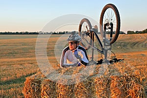 The cyclist with the bike resting on straw harvested field