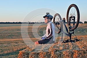 The cyclist with the bike resting on straw harvested field