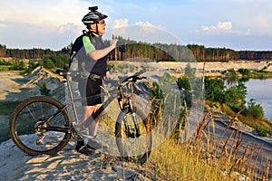 The cyclist with the bike on a sand quarry with binoculars in hand
