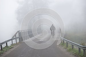 Cyclist on bridge in heavy fog on gloomy autumn day