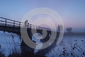 cyclist crossing misty bridge at dawn