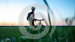 Cyclist on green meadows on summer evening under sunset. Fitness concept