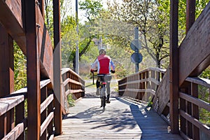 cyclist with helmet riding his mountain bike crossing a wooden brown bridge in a sunny day. Rider wears a red sweeter. Horizontal