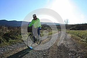 A cyclist on macadam country road with sun light behind him