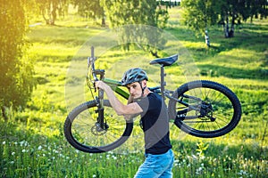 Cyclist man in helmet carries his mountain bike in the rise in the background green nature. Active and healthy lifestyle
