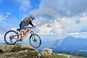 Cyclist man riding electric mountain bike outdoors along grassy trail in the mountains.