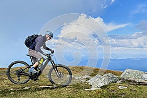 Cyclist man riding electric mountain bike outdoors along grassy trail in the mountains.