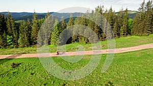 Cyclist man riding electric mountain bike outdoors along grassy trail in the mountains.