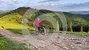 Cyclist man riding electric mountain bike outdoors along grassy trail in the mountains.