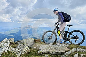 Cyclist man riding electric mountain bike outdoors along grassy trail in the mountains.