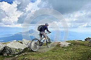 Cyclist man riding electric mountain bike outdoors along grassy trail in the mountains.