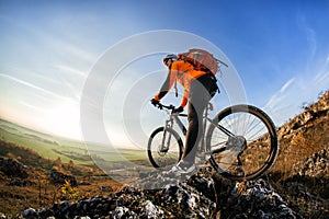 Cyclist man standing on top of a mountain with bicycle and enjoying valley view on a sunny day against a blue sky