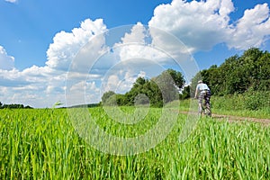 Cyclist moves on a dirt road Lane in meadow and deep blue sky