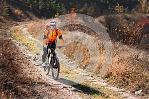 Cyclist in the orange jacket riding a bike on countryside road at the sunrise.