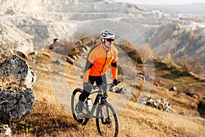 Cyclist in Orange Jacket Riding the Bike Rocky Hill. Extreme Sport Concept. Space for Text.