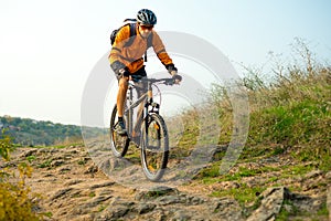 Cyclist in Orange Riding the Mountain Bike on the Autumn Rocky Trail. Extreme Sport and Enduro Biking Concept.