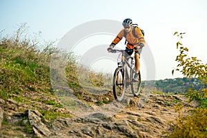 Cyclist in Orange Riding the Mountain Bike on the Autumn Rocky Trail. Extreme Sport and Enduro Biking Concept.