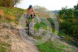 Cyclist in Orange Riding the Mountain Bike on the Autumn Rocky Trail. Extreme Sport and Enduro Biking Concept.