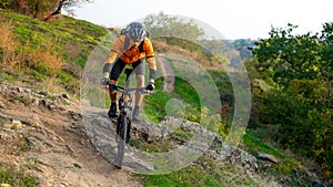 Cyclist in Orange Riding the Mountain Bike on the Autumn Rocky Trail. Extreme Sport and Enduro Biking Concept.