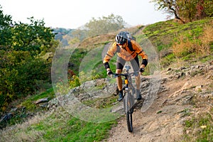 Cyclist in Orange Riding the Mountain Bike on the Autumn Rocky Trail. Extreme Sport and Enduro Biking Concept.