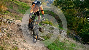 Cyclist in Orange Riding the Mountain Bike on the Autumn Rocky Trail. Extreme Sport and Enduro Biking Concept.