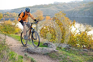 Cyclist in Orange Riding the Mountain Bike on the Autumn Rocky Trail. Extreme Sport and Enduro Biking Concept.