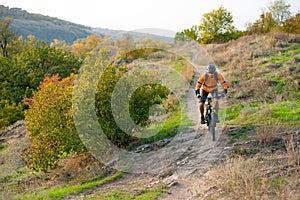 Cyclist in Orange Riding the Mountain Bike on the Autumn Rocky Trail. Extreme Sport and Enduro Biking Concept.