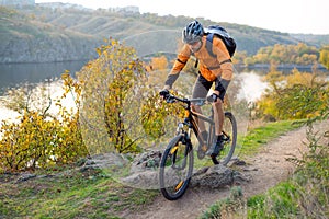 Cyclist in Orange Riding the Mountain Bike on the Autumn Rocky Trail. Extreme Sport and Enduro Biking Concept.