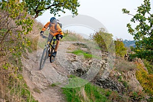 Cyclist in Orange Riding the Mountain Bike on the Autumn Rocky Trail. Extreme Sport and Enduro Biking Concept.