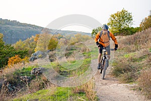 Cyclist in Orange Riding the Mountain Bike on the Autumn Rocky Trail. Extreme Sport and Enduro Biking Concept.