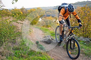 Cyclist in Orange Riding the Mountain Bike on the Autumn Rocky Trail. Extreme Sport and Enduro Biking Concept.